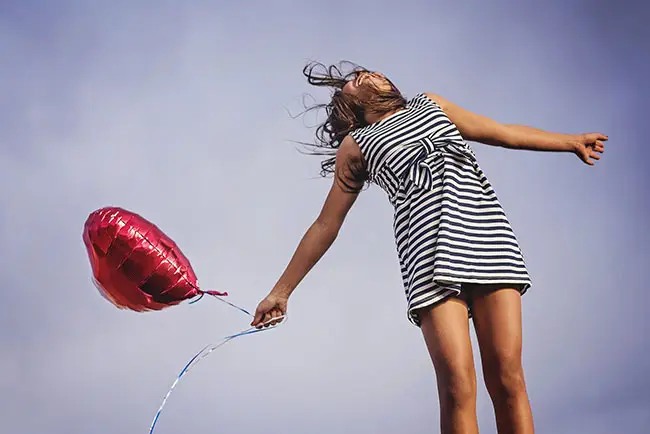 donna felice salta nell'aria con in mano un palloncino a forma di cuore