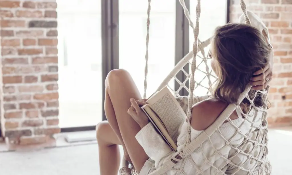 donna legge un libro su una sedia sospesa in macramè