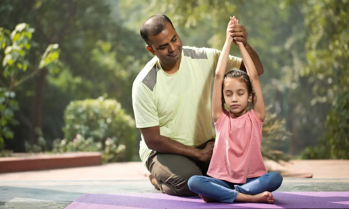uomo di mezza età aiuta una bambina a mantenere la giusta postura in un asana yoga