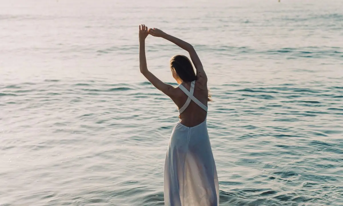 Donna in abito elegante che danza in riva al mare