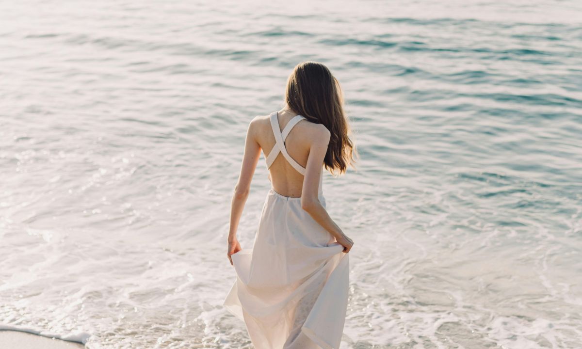 Donna in abito bianco che cammina sulla riva del mare al tramonto