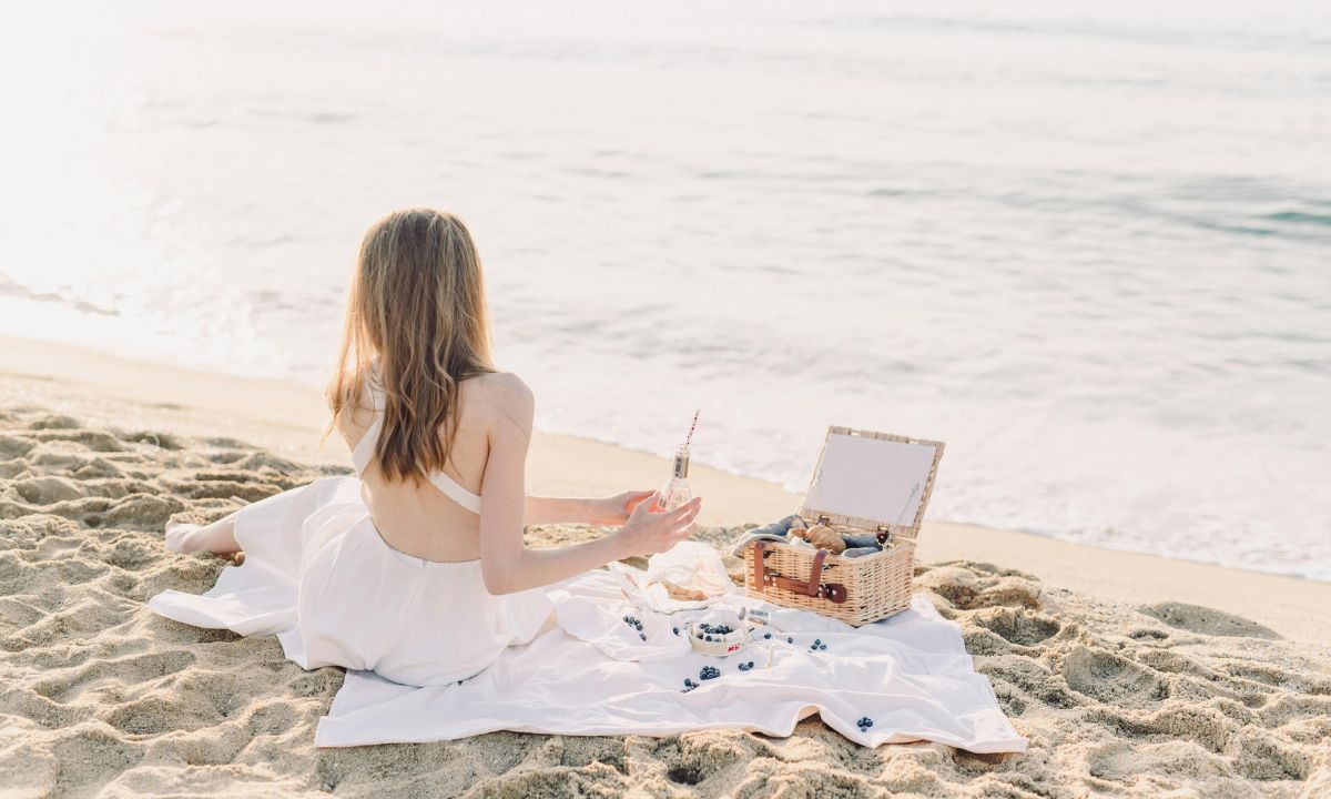 Donna seduta in meditazione sulla spiaggia con un cesto da picnic accanto a lei